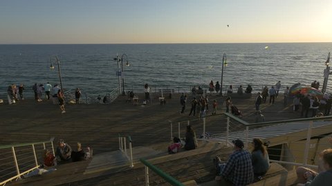 Santa Monica, United States - June, 2017: Tourists relaxing on a pier at sunset