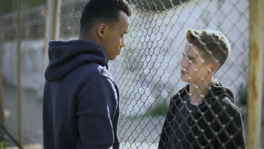 Two boys of different nationalities talking, rich and poor separated by fence Royalty-Free Stock Footage #1015351363