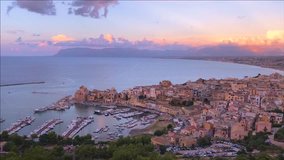 A beautiful sunset on the coast of Italy. An ancient city on the mountains, the sea, yachts. High mountains, airy clouds. Castellammare del Golfo, Sicily, Italy. Time lapse. Aerial view