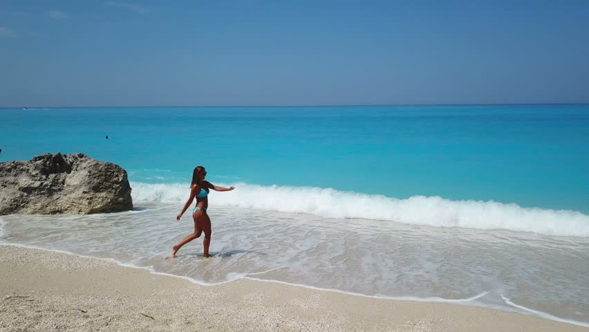 Beautiful happy young woman walking on the beach in the water