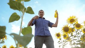 man farmer working holding in hand a plastic bottle sunflower oil stands in the field. slow motion video. sunflower oil production and research agriculture farming. large sunflowers against the blue