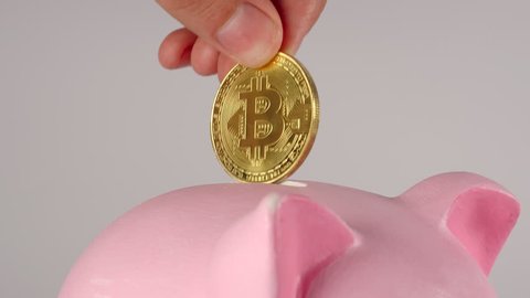 CLOSE UP: Male hand throws bitcoin into a pink piggy moneybox