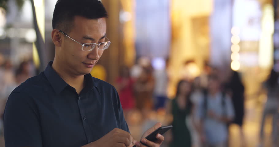 Happy young asian man looking at his mobile phone in street at night,4k