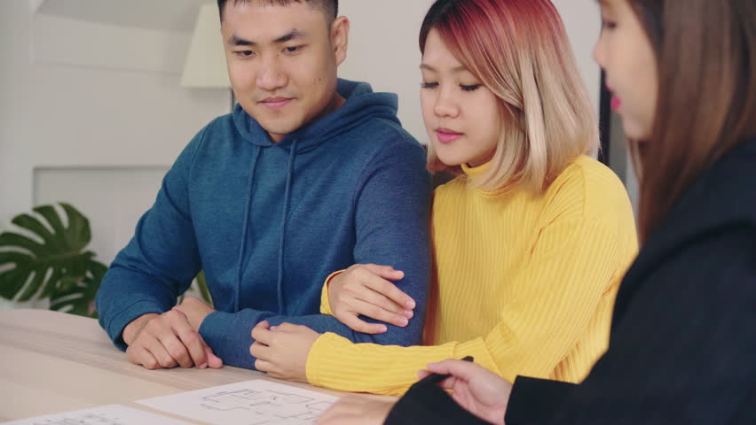 Happy young Asian couple and realtor agent. Cheerful young man signing some documents while sitting at desk together with his wife. Buying new house real estate.   Royalty-Free Stock Footage #1015377007