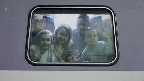 Four people family wave hands near window of train