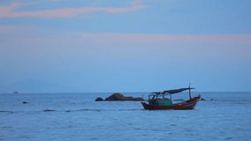 Fisherman in a small wooden fishing boat navigating across the south china sea, under tropical sunset skies high definition stock footage clip.