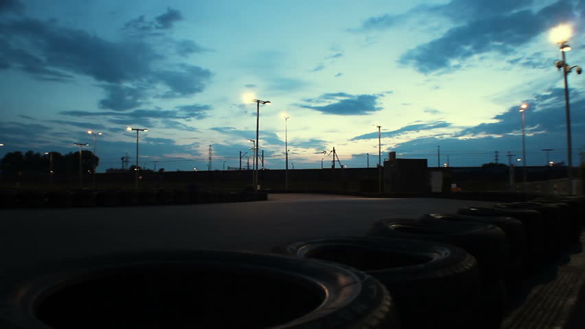 Outdoor go-kart track with cars passing under dark blue evening sky, time-lapse