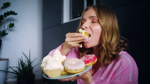 Eating woman enjoy cream cupcake. Food calories. Close up hungry overeating young girl eating cake with big appetite. Portrait of eating girl with sweet cake. Woman tasting sweet cookies
