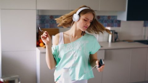 Sexy girl dancing at home. Dancing woman eating cornflakes breakfast in kitchen. Expressive girl having fun in morning. Dancing girl listening music in headphones. Enjoying new day