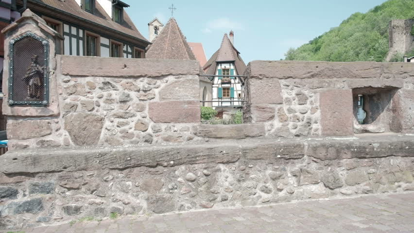 Camera forward push-in stone bridge wall rampart to reveal traditional half-timbered houses and river in the picturesque medieval French village of Kaysersberg, France