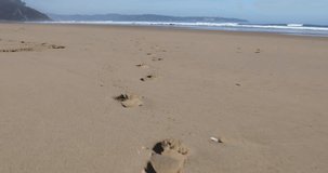 4k video following footprints both feet on sand of Vega Beach seaside next to Ribadesella, Asturias, Spain, Europe
