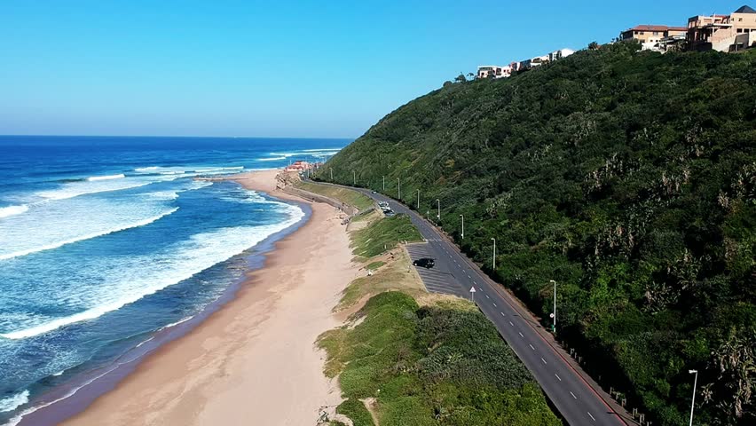 Aerial view of the beach, deep blue water, crashing waves and coast road with passing cars. Durban, South Africa.