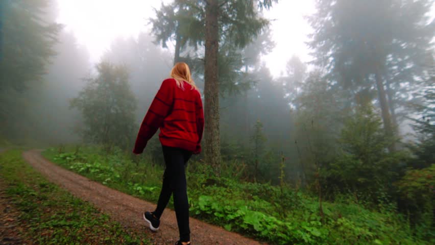 SLOWMO, following girl in red sweater through a misty forest trail