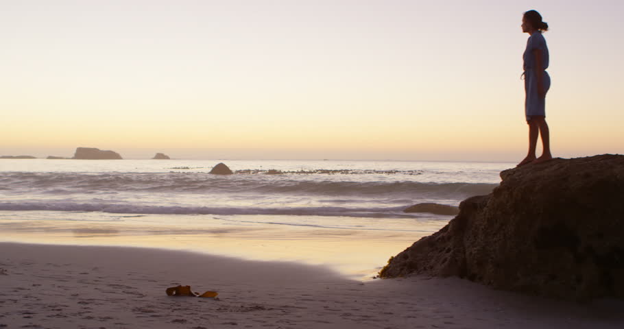Woman relaxing on a rock in the beach at dusk 4k