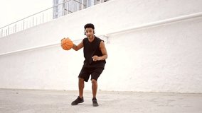Happy african man in headphones playing in basketball outdoors and looking at the camera