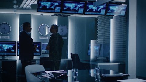 Federal Special Agent Talks To Military Man in the Monitoring Room. In the Background Busy System Control Center with Monitors Showing Data Flow. Shot on RED EPIC-W 8K Helium Cinema Camera.