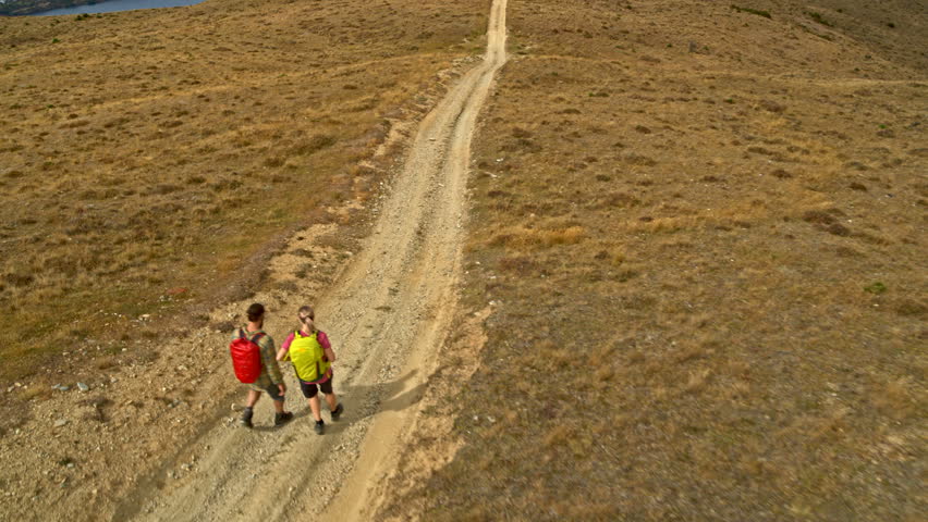 Aerial drone of Caucasian adventure hikers with backpack trekking on mountain road Mount Aspiring Lake Wakatipu New Zealand