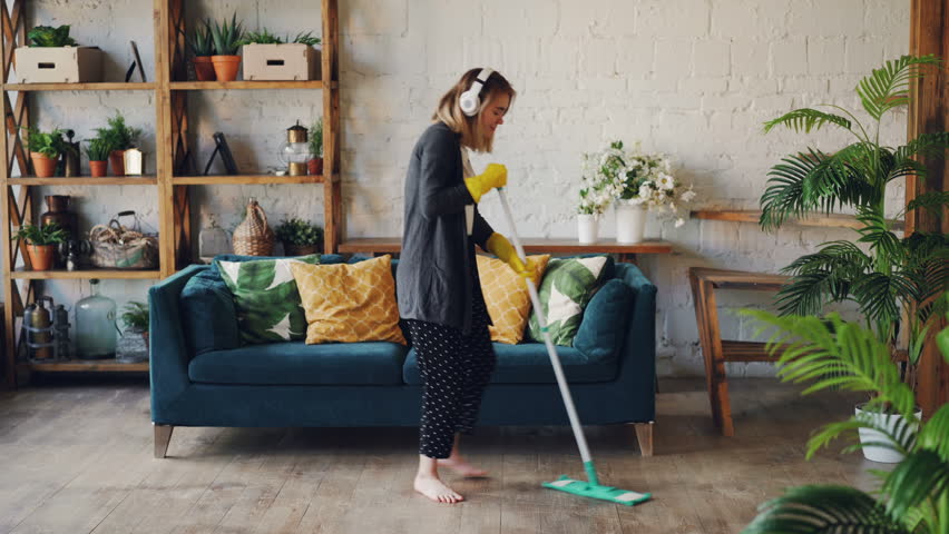 Attractive girl in headphones is listening to music and dancing wih mop during domestic work, she is mopping floor at home and having fun. Women, joy and houses concept. Royalty-Free Stock Footage #1015401439