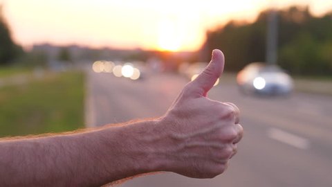 Man hand close up thumb up, hitchhiker on road try to catch car, traffic pass by