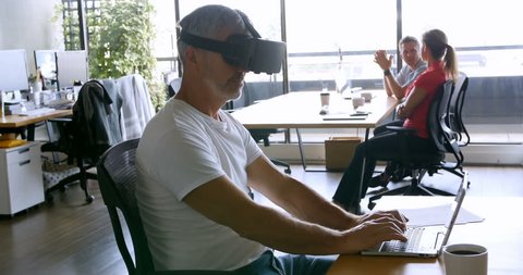 Male executive using virtual reality headset and laptop at desk in the office 4k