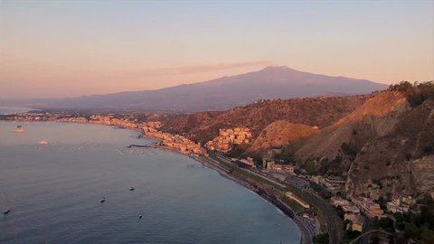 View of the city of Taormina and active volcano Etna at sunrise. Delightful morning scenery on the town of Taormina and the volcano Etna. Sicily, Italy