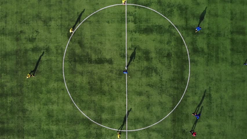 Aerial football match start. Beginning of game. Aerial shot Two teams playing ball in football outdoors, top view. Football game outdoors, green field with markings, players running around with a ball