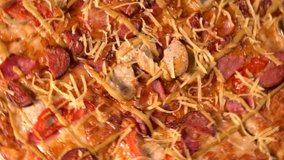 Overhead view of a spinning homemade pizza with mushrooms, meat, tomatoes and cheese on a thin crispy crust in a close up view