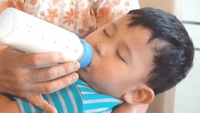 Boy in mother chest drinking milk from bottle while sleeping