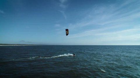 In this aerial drone camera shot you can see fearless extreme sport lover - kiteboarder riding ocean water with his kite flying in the blue sky.