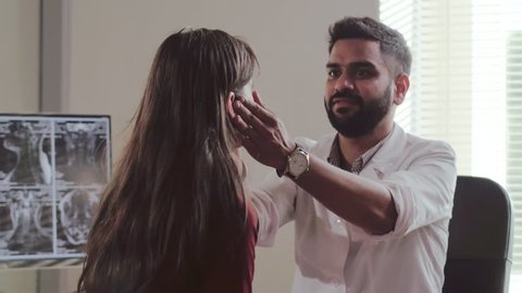 Caucasian young girl visit to doctor dermatologist. Attractive indian male doctor checks eyes and eyeballs of female patient. Examination of patient 스톡 비디오