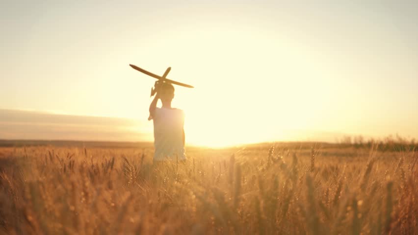 Happy kid runs with a toy airplane in a wheat field at sunset. Kid dreams of becoming an airplane pilot. Toy airplane in the hands of  child. Happy kid runs at sunset, holding the plane. Pilot-aviator | Shutterstock HD Video #1015426687