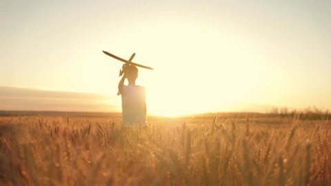 Happy kid runs with a toy airplane in a wheat field at sunset. Kid dreams of becoming an airplane pilot. Toy airplane in the hands of  child. Happy kid runs at sunset, holding the plane. Pilot-aviator