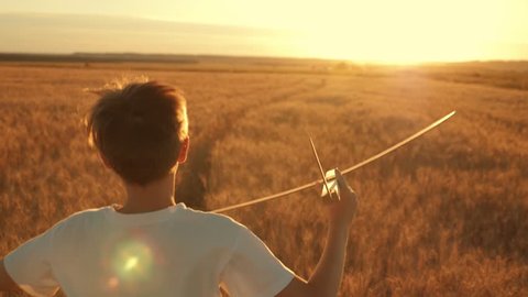 Happy kid run with a toy airplane at sunset over a wheat field. The kid dreams of becoming an astronaut pilot. Airplane pilot. Children's dream to run with a toy. Kid airplane pilot. Dream concept