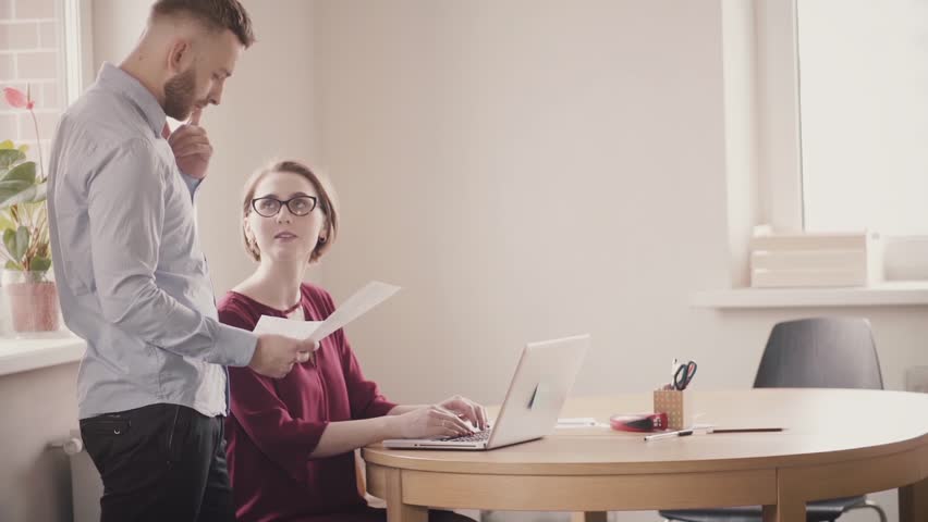 Young European man and woman cooperate by the table at modern office, talk and smile. Teamwork in healthy workplace | Shutterstock HD Video #1015433833