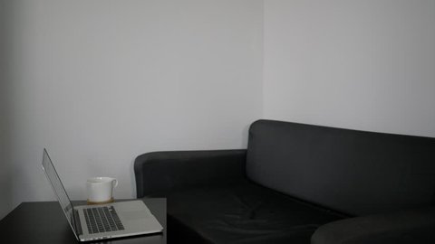 A young man works at a laptop sitting on a black couch.