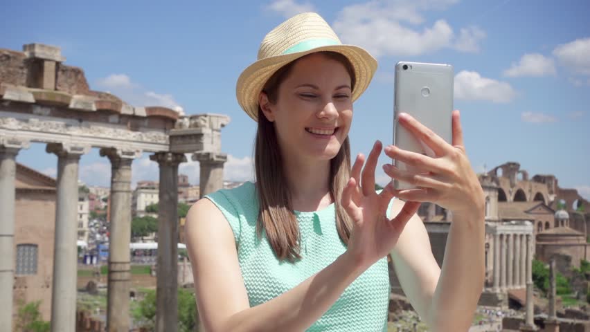 Woman near ancient ruins Forum Romanum using mobile phone in slow motion. Female tourist having video chat via online app against Roman forum in center of Rome, Italy. Student travel through Europe