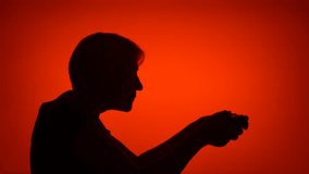Silhouette of senior woman gamer playing video game online. Female's face in profile with game console on red background. Black contour shadow of grandmother's half-face winning computer game