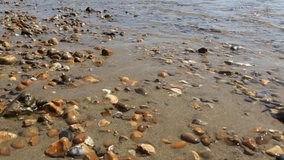 Tilt up from pebbles to small waves on beach in Lyme Regis, Dorset