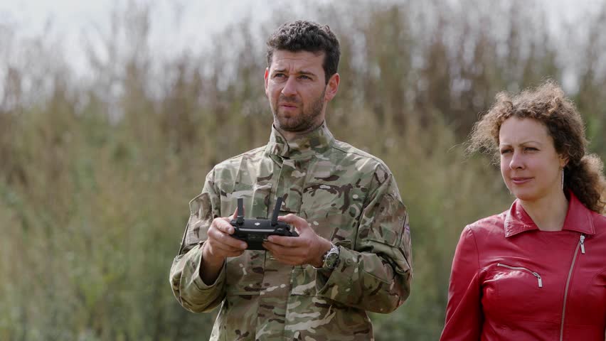 Woman stands near military man with drone remote in warm air at autumn day