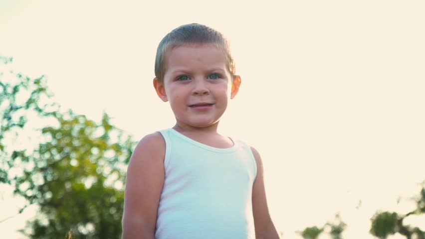 4-year-old boy in a white t-shirt laughs, kid jumps up and shows the class on his fingers. Portrait of a cheerful active child on a nature background.