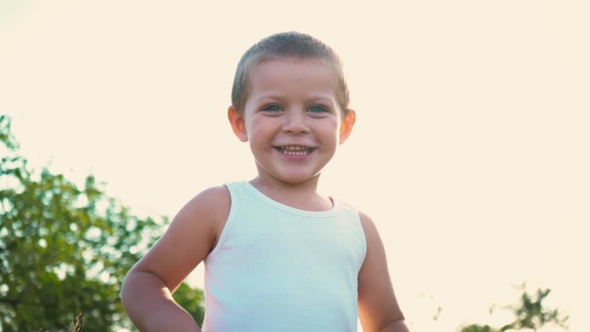 4-year-old boy in a white t-shirt laughs and stretches out his hands. Portrait of a cheerful active child on a nature background.
