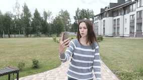 Beautiful brunette woman blogger talk a video chat on mobile phone walking near the home.