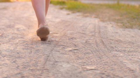 Woman feet in flat shoes walk on dust road at hot summer day