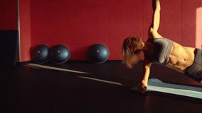 Woman doing a Side plank for abdominal workout on blue mat. This Video about fitness. Sunset light.