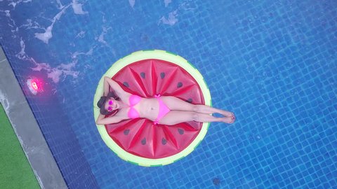  Top view of a woman in bikini suit on the unicorn floating rubbers. To enjoy the relax time in swimming pool on vacation at the hotel or resort
