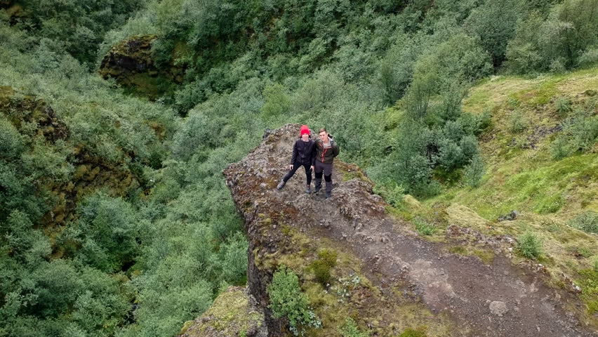Aerial view of couple of hikers standing on the edge of a cliff on Thorsmork mountain ridge trail in Iceland. Drone mowing from them