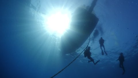 scuba divers ascending underwater to  the boat underwater surface background sun shine beam and rays
