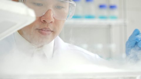 Close-up of a Medical research scientist takes out petri dish with frozen samples of cells from a cryogenic nitrogen container in a science research lab. He works in a busy modern laboratory center. 
