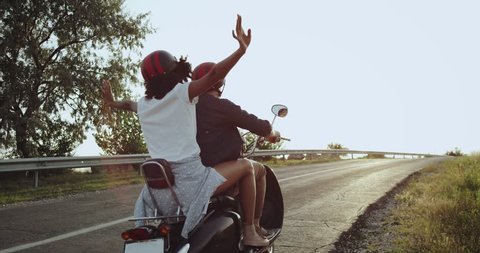 The girl on the motorbike is waving her hands into the air being all excited going on a long distance journey with her lover