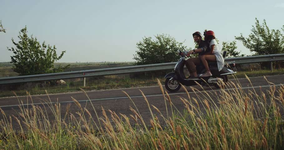 The view from a field full of grass and field weeds all you see is a couple riding their motorbike smoothly all inlove and happy4k